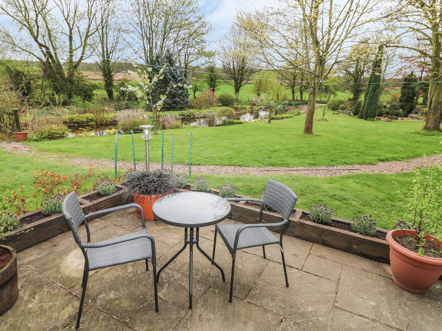 Een terras met een ronde tafel en vier stoelen, omgeven door verhoogde bloembedden en diverse planten.
