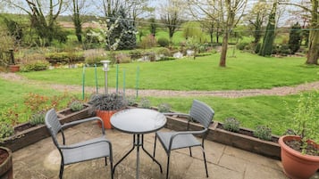 Een terras met een ronde tafel en vier stoelen, omgeven door verhoogde bloembedden en diverse planten.