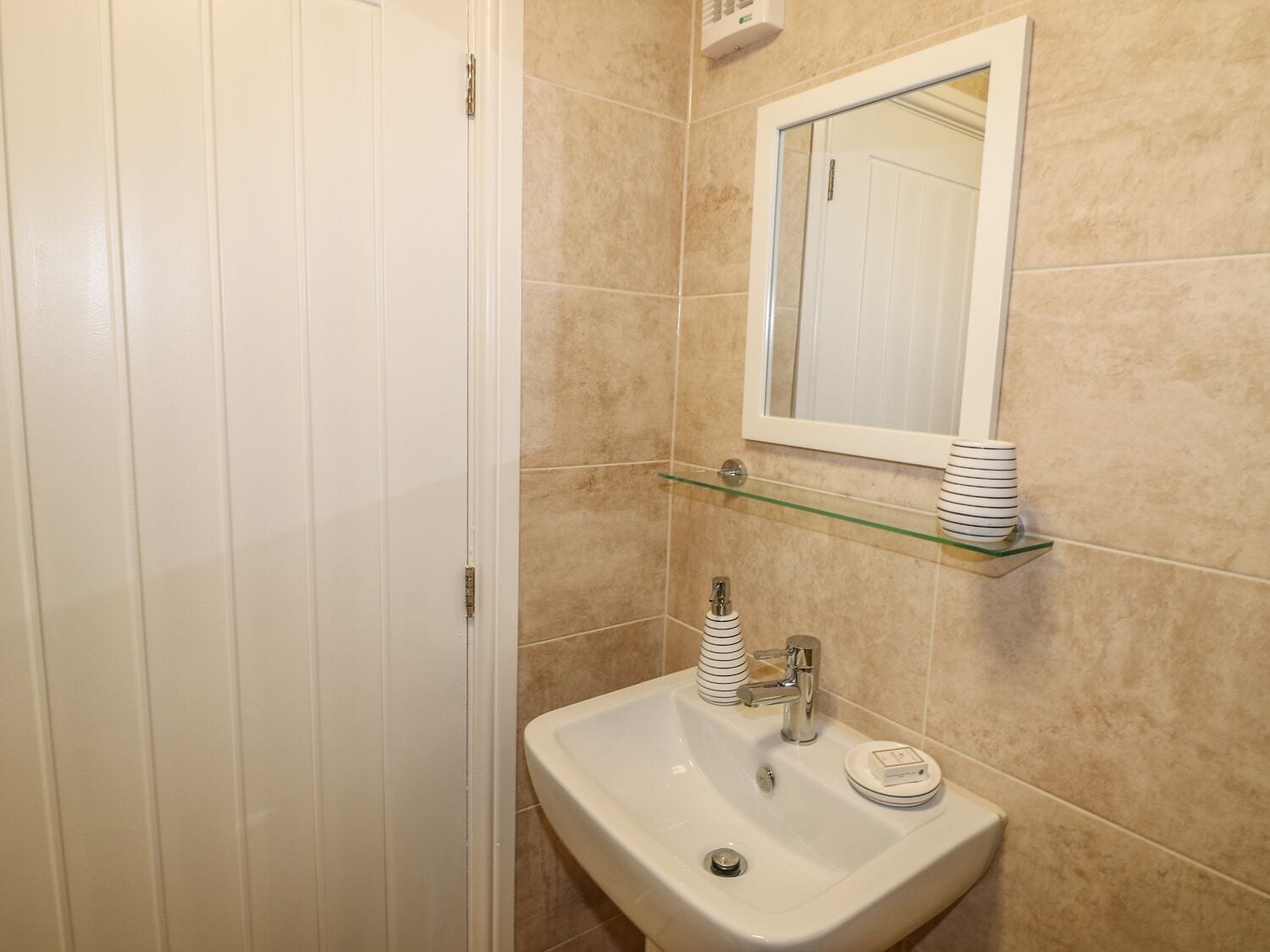 A bathroom with a white sink, a mirror, and a glass shelf with stacked plates.