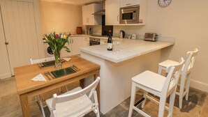 Cozinha compacta com ilha central, armários brancos, micro-ondas e relógio na parede.