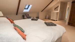Quarto com uma cama grande, claraboia, cadeira, cômoda e espelho.
