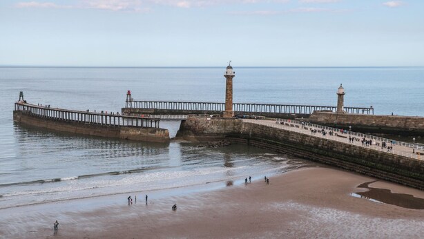 A coastal pier with a lighthouse, a sandy beach, and a calm sea. - Seahorse (Whitby)
