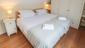 A bedroom with two beds, a wardrobe, a nightstand, and bedside lamps. - Seahorse (Whitby)