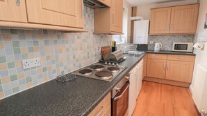 A compact kitchen with wooden cabinets, a black countertop, a built-in stove, and a microwave. - Seahorse (Whitby)