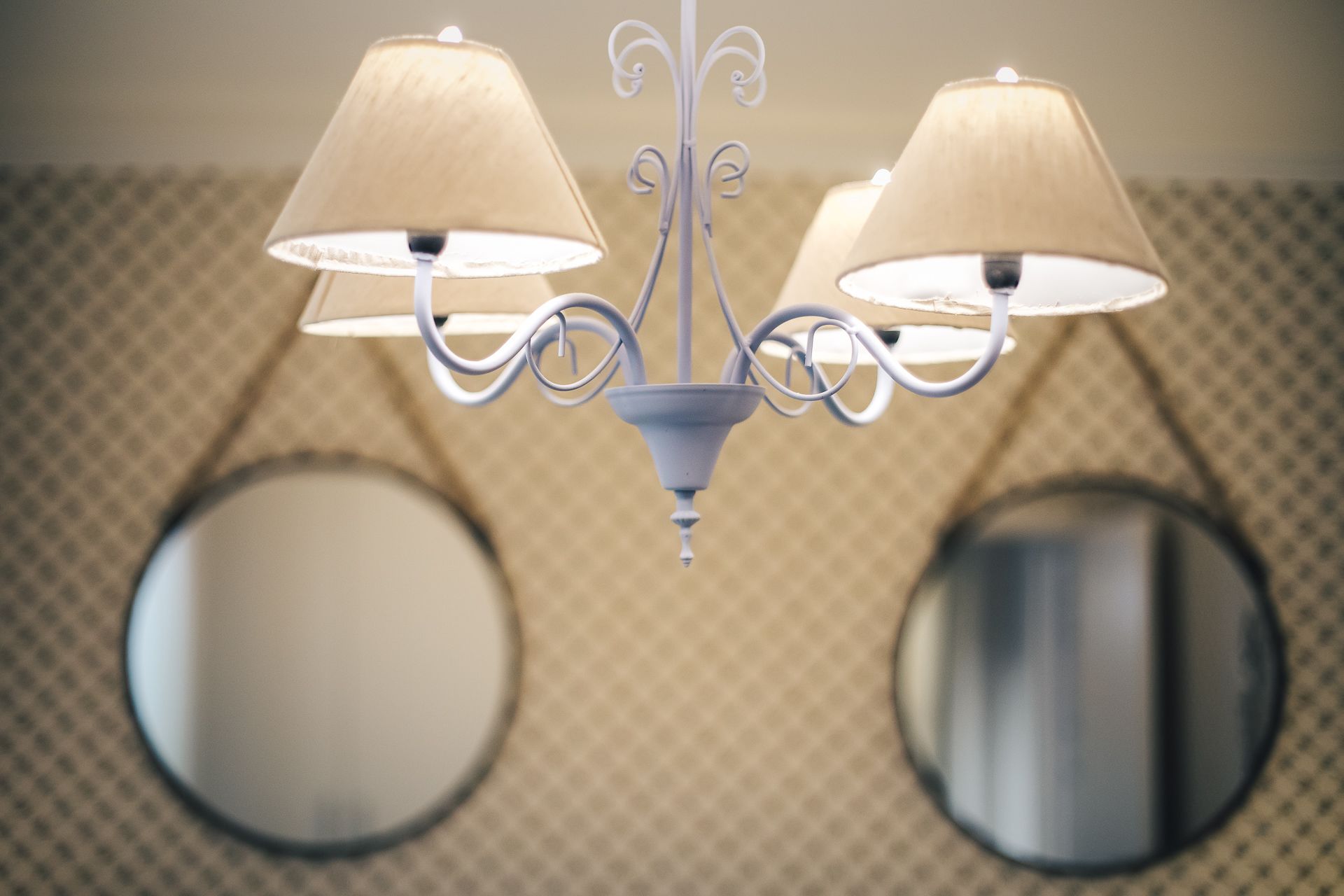 A chandelier with three lampshades and two round mirrors below it.