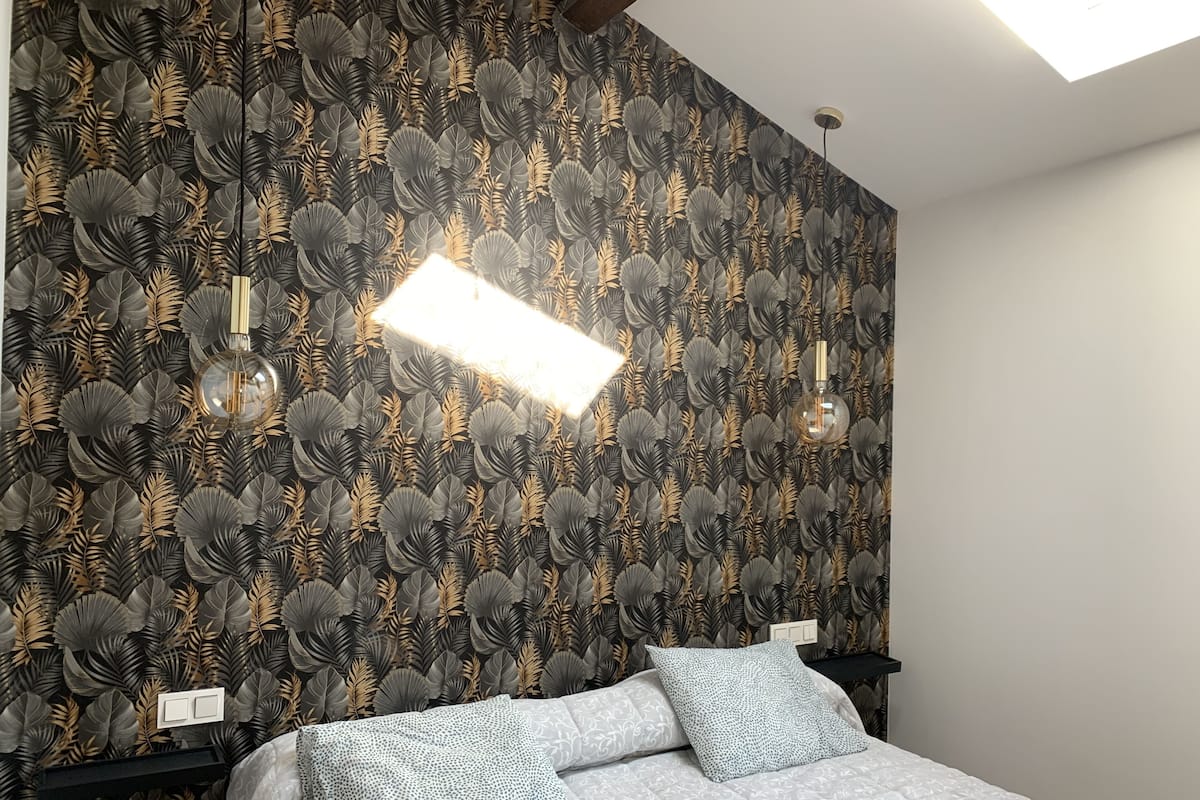 Ein Schlafzimmer mit gemustertem Wandpapier, einem Bett mit Kissen und einer Deckenleuchte.