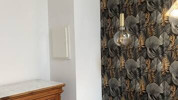 Un dormitorio con un aparador de madera, una cama con un cojín estampado y un papel tapiz con motivos de hojas.