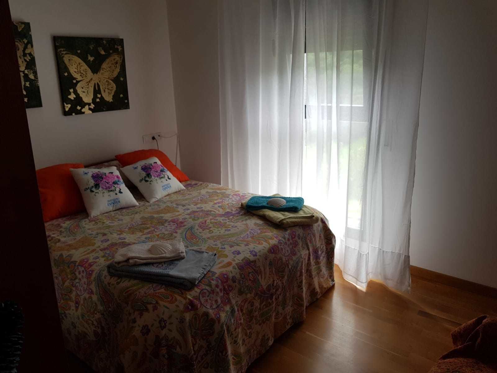 A bedroom with a bed, pillows, a blanket, and a window with sheer curtains.
