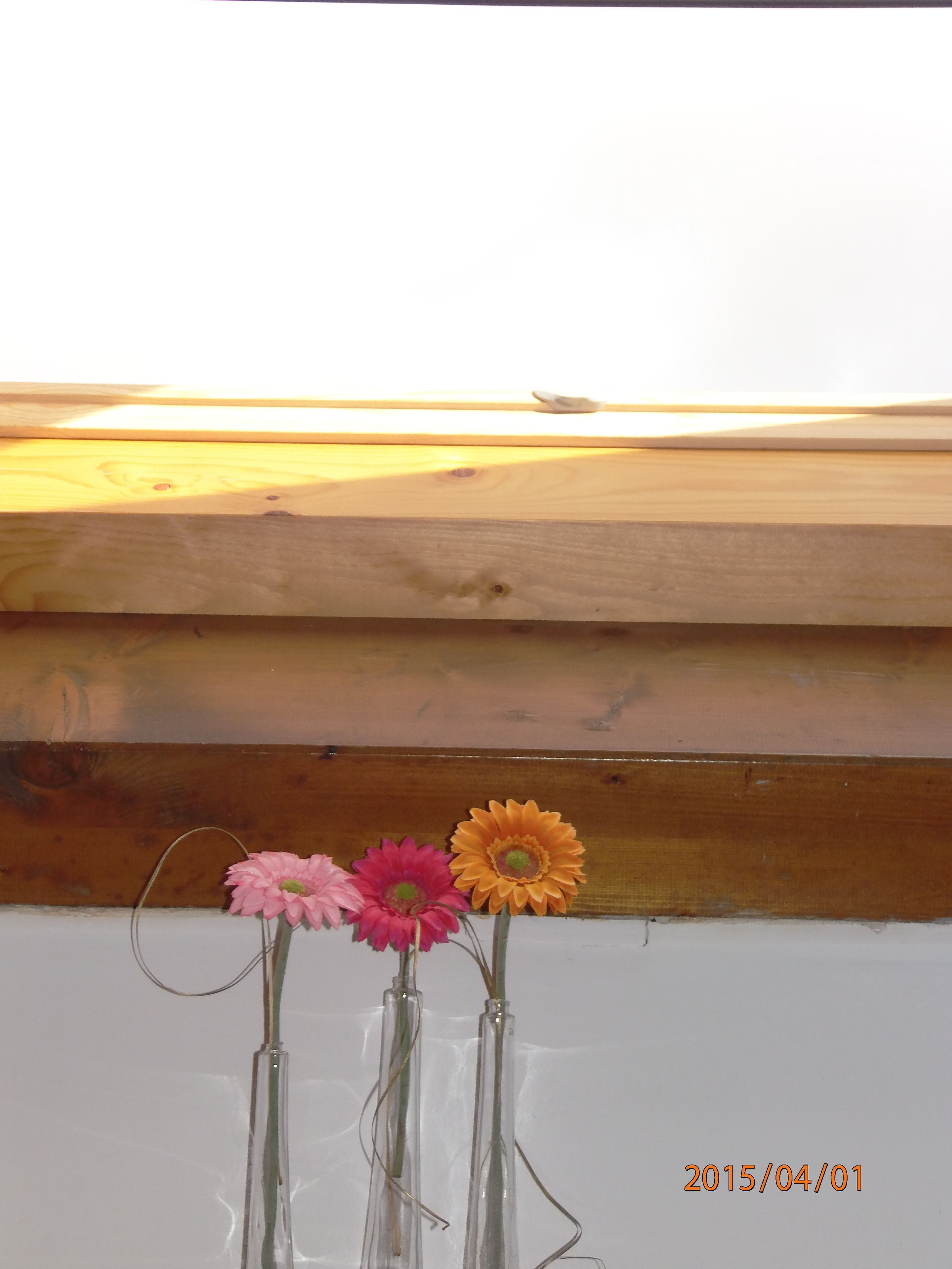 Trois vases en verre ornés de fleurs, posés sur une surface blanche.