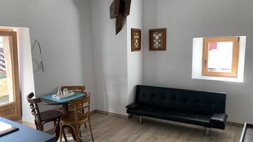 Una habitació amb taula de menjador, cadires, un sofà negre i una finestra amb vistes.