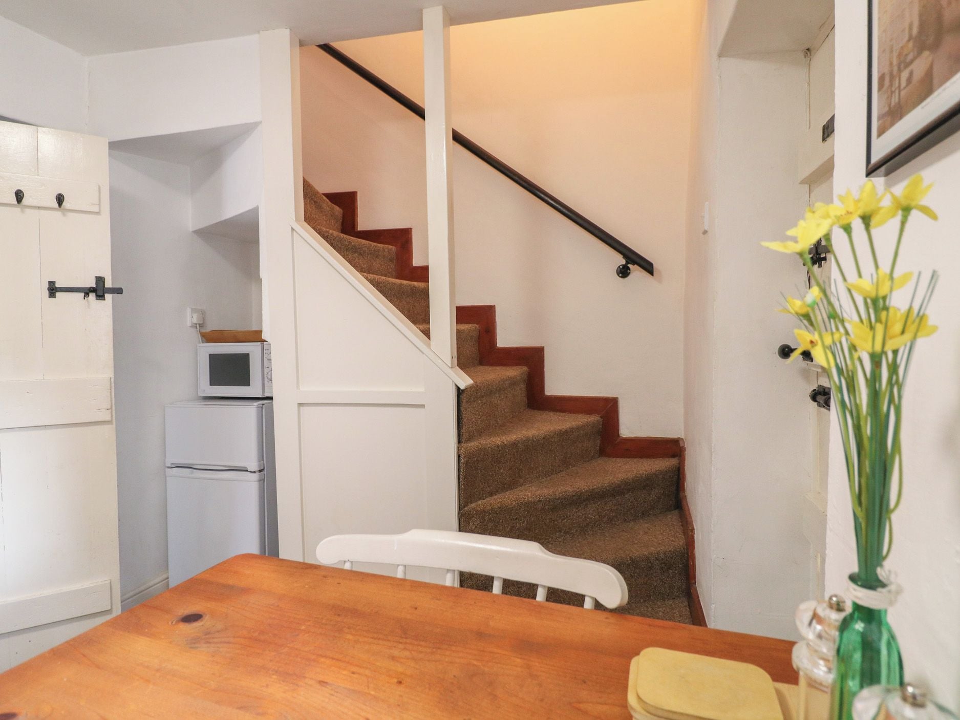 A kitchen with a wooden table, white chairs, a refrigerator, and a staircase with a wooden railing.