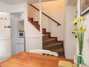 Una cocina con una mesa de madera, sillas blancas, un refrigerador y una escalera con barandilla de madera.