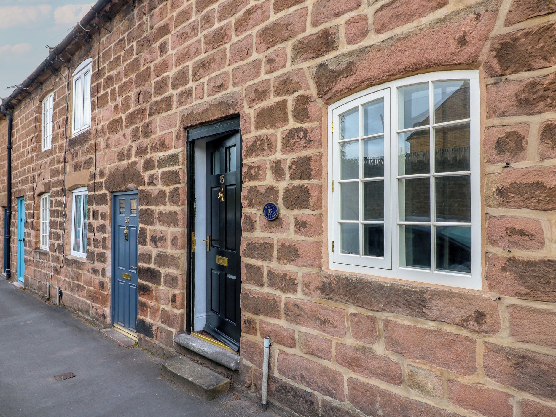 Kivinen rakennus, jossa on musta ovi, sininen ovi ja valkoisilla kehyksillä varustettu ikkuna.