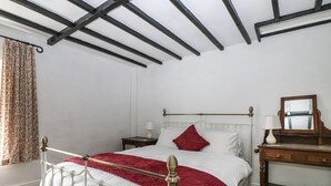 Een slaapkamer met een bed met een wit metalen frame, een rode spreideken, een houten dressoir met spiegel en een nachtkastje met een lamp.