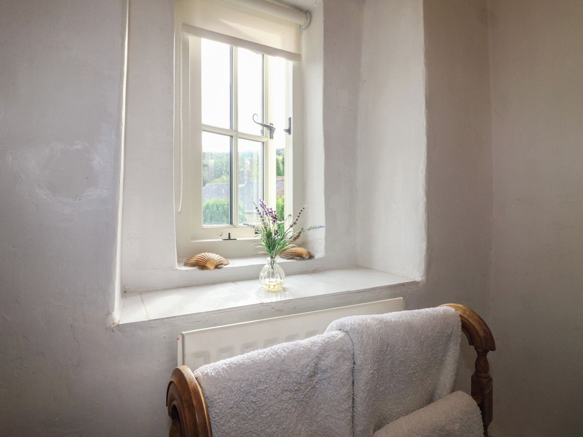 Un baño con ventana, un perchero y un jarrón pequeño con flores.
