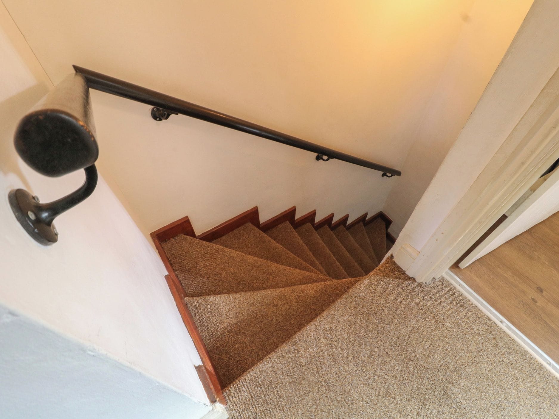 Un escalier recouvert de moquette, doté d’une rampe et d’une porte en bas.