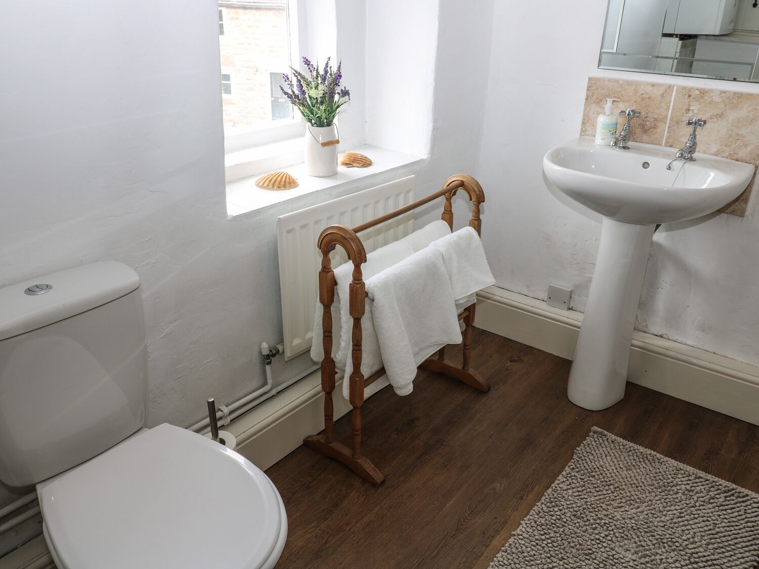 A bathroom with a toilet, a wooden towel rack, a sink, and a window with a plant.