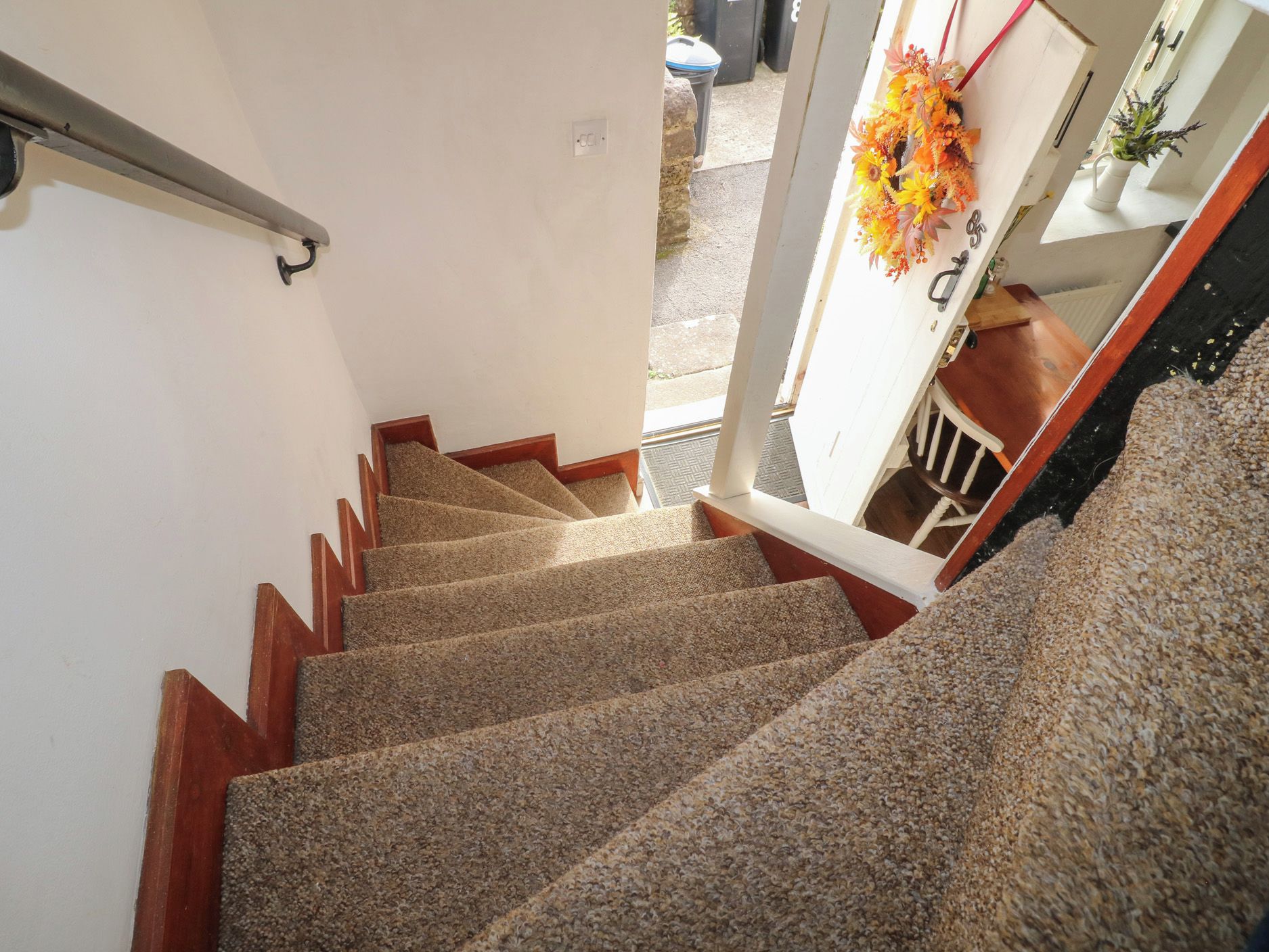 A carpeted staircase with wooden handrails and a door leading outside.