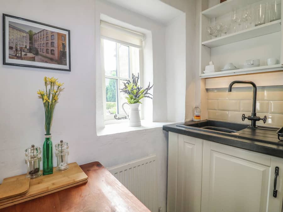 A kitchen with white cabinets, a black countertop, a window with a view of greenery, and a vase with flowers on the windowsill.