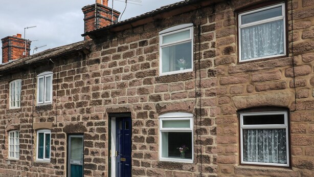 A stone-built row house with multiple windows, a blue door, and a visible chimney. - The Hill (Matlock)
