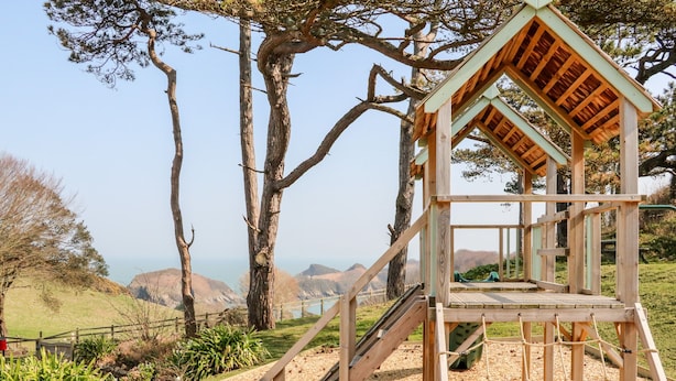 A wooden observation tower with a staircase and a viewing platform, surrounded by trees and a scenic landscape. - Martin Cottage (Ilfracombe)