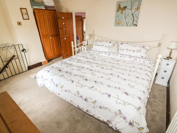 A bedroom with a floral bedspread, wooden wardrobe, and a painting of butterflies. - Megs Cottage (Norwich)