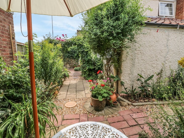 Un chemin de jardin bordé de plantes en pot et surmonté d’une table blanche.