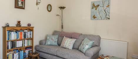 A cozy living room with a grey sofa, a wooden bookshelf, and a patterned rug.