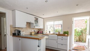 A kitchen with white cabinets, a wooden countertop, and a window overlooking a brick wall.