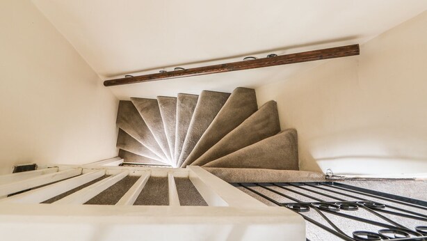 A spiral staircase with a wooden handrail and carpeted steps.