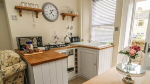 Una cucina compatta con piano di lavoro in legno, forno integrato e lavandino. Sopra al bancone, scaffali con barattoli e utensili da cucina.