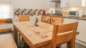 A modern kitchen with white cabinets, a wooden dining table, and a built-in microwave. - Little Byre Cottage (Thirsk)