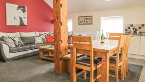 A living room with a red wall, a wooden dining table, and a sofa. - Little Byre Cottage (Thirsk)