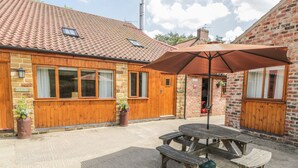 A rustic building with a tiled roof, wooden exterior, and a patio area with a table and benches. - Little Byre Cottage (Thirsk)