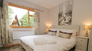 A bedroom with a large bed, plaid carpet, a window with curtains, a radiator, and a painting on the wall.