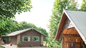 A rustic wooden cabin with a gravel driveway, a small porch, and a dining area with outdoor seating.