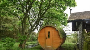 A wooden cabin with a circular design, a wooden door, and a small window. There is a wooden pathway leading to the cabin.