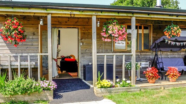A wooden cabin with a porch, a small entryway, and hanging flower baskets.