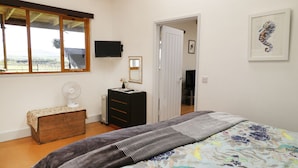 A bedroom with a bed, a dresser, a mirror, a TV, and a window with a view of the outdoors.
