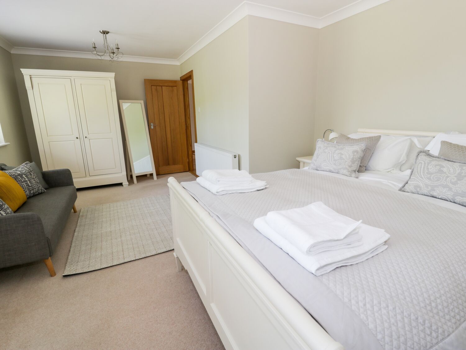 A bedroom with a bed, a grey sofa, a wardrobe, and a door.