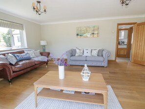 Un salón con un sofá de cuero marrón, un sofá gris, una mesa de centro de madera y un jarrón blanco con flores.