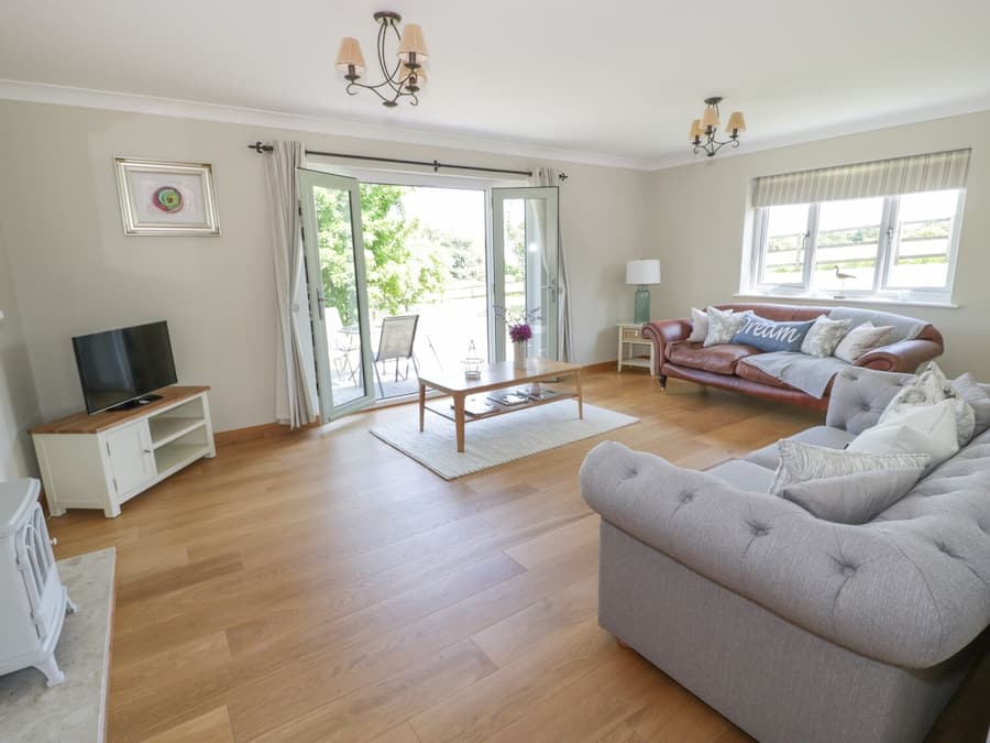 A spacious living room with a sofa, a coffee table, a TV on a cabinet, and a sliding glass door leading to an outdoor area.