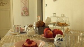 Una mesa de comedor dispuesta con un mantel de encaje, un bol de fresas, un plato de manzanas y un vaso de agua.