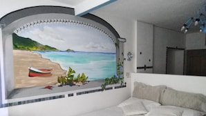 Un dormitorio con cama, un mural en la pared que representa una playa y una puerta.