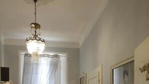Una habitación con candelabro, una silla, una mesita con flores, un espejo y un cuadro en la pared.