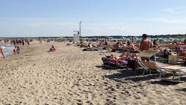 Una playa concurrida, gente caminando y tomando el sol.