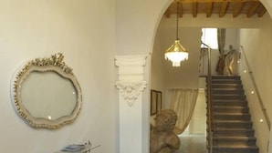 Un pasillo con una escalera de madera, un candelabro y una escultura de piedra.