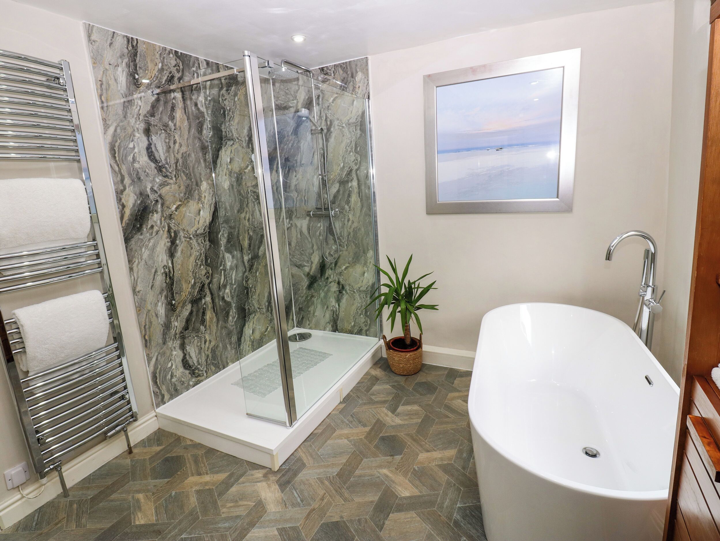 A modern bathroom with a glass-enclosed shower, a freestanding bathtub, and a potted plant.