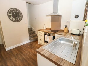 Una cocina compacta con encimera de madera, un lavamanos de acero inoxidable, un horno integrado y un reloj en la pared.