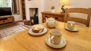 Ein gemütliches Wohnzimmer mit Kamin, Fernseher, Esstisch mit Kuchen und Teekanne sowie einer Lampe.